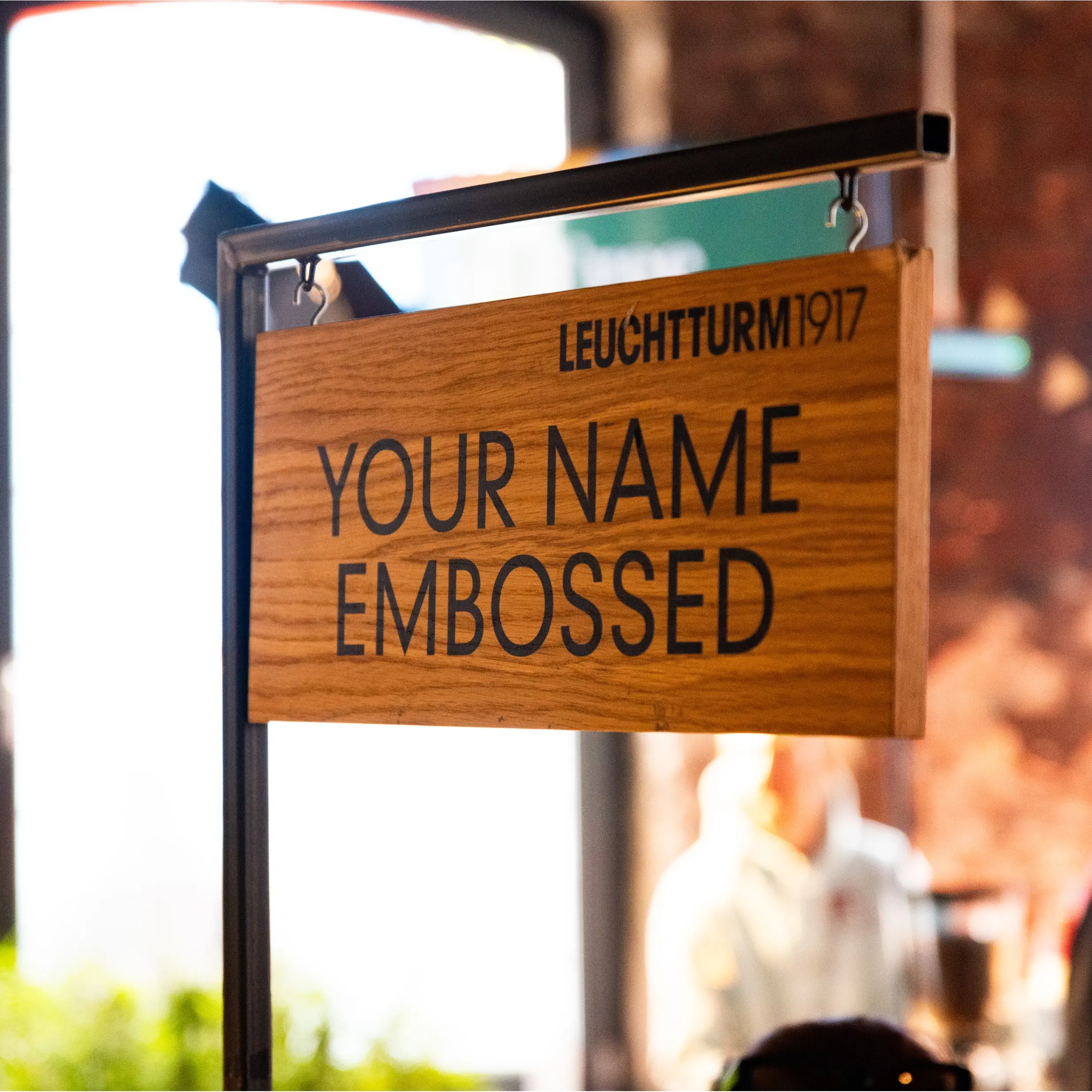 Cartel de madera con texto «YOUR NAME EMBOSSED» en un stand.